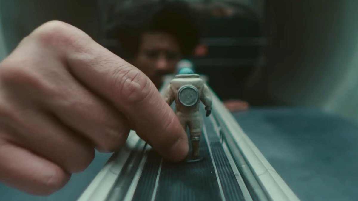 A hand holds a little astronaut figure on a model ramp as Victor Timely watches from the end of the ramp on Loki